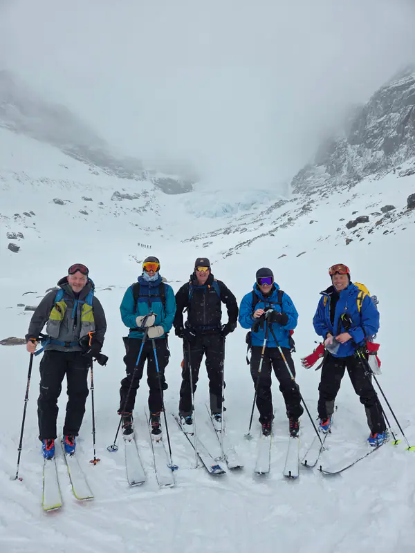 Gruppe med toppturski samlet under snødekt fjellside
