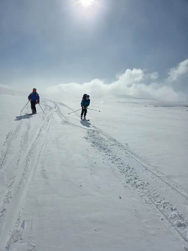 Skiløpere på vei opp snøvidde i motlys